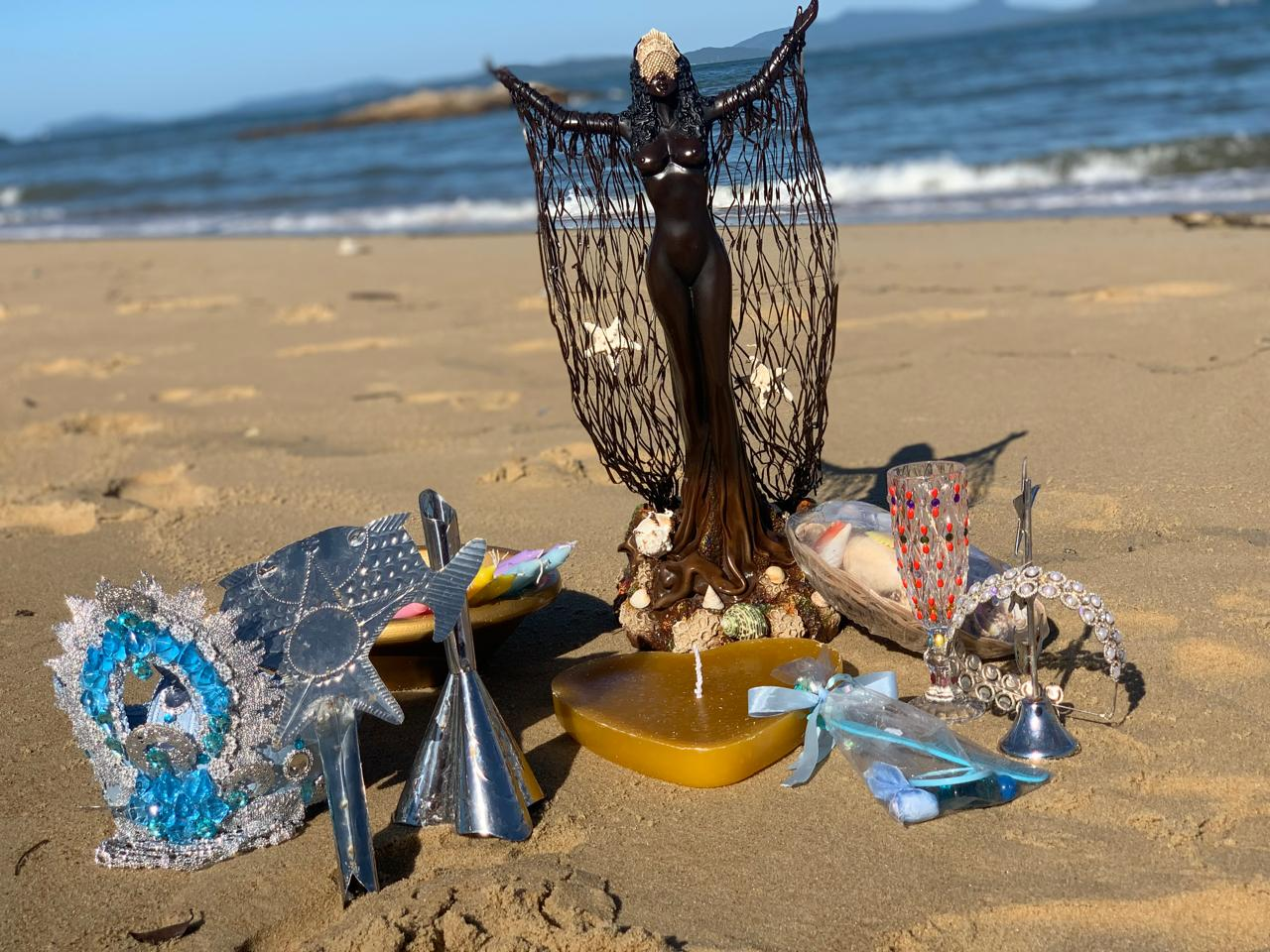 Oferenda de mar com imagem, velas e flores na areia ao amanhecer